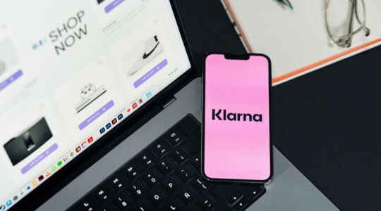 Telefoon met het Klarna-logo naast een laptop met een open online webshop, illustratie van achteraf betalen