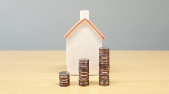 Een huisje met stapeltjes geld ervoor.