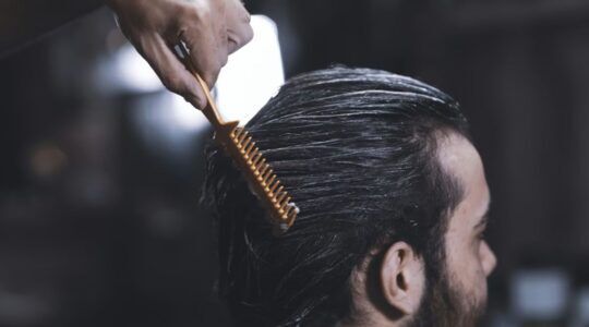 Een man die zit en iemand die zijn haar kamt.