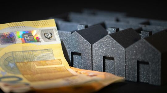 Een stapel eurobriefjes naast een drietal miniatuur huisjes