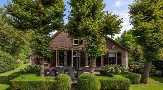 Een huis met bomen ervoor en omringd door een tuin.