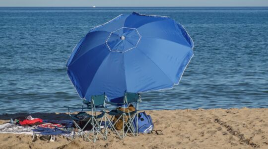 Een strand met een parasol, stoeltjes en een handdoek.