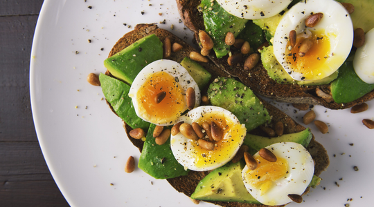 Een broodje op een bord met avocado, ei en pitten.